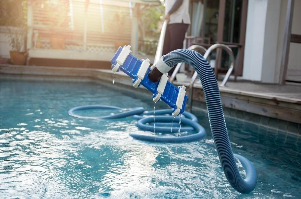 Man using a vacuum tube cleaner to remove debris from a pool.