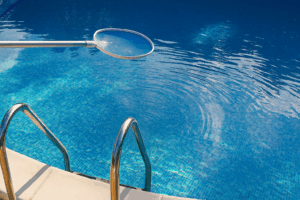 A clean, sparkling blue swimming pool with a metal ladder and a skimmer net gently stirring the water, highlighting the clarity and maintenance of the pool