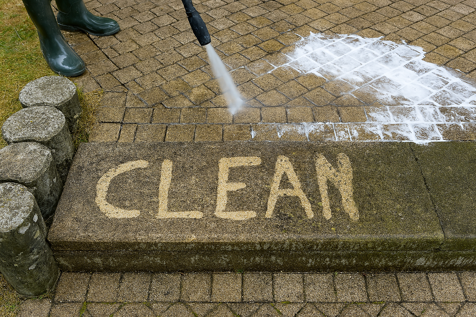 Pressure washing stone pavers with the word CLEAN revealed