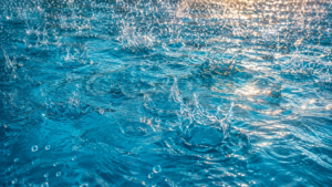 Pool water after rain shown by bright raindrops creating crisp circular splashes across clear blue water during an Orlando sunshower.