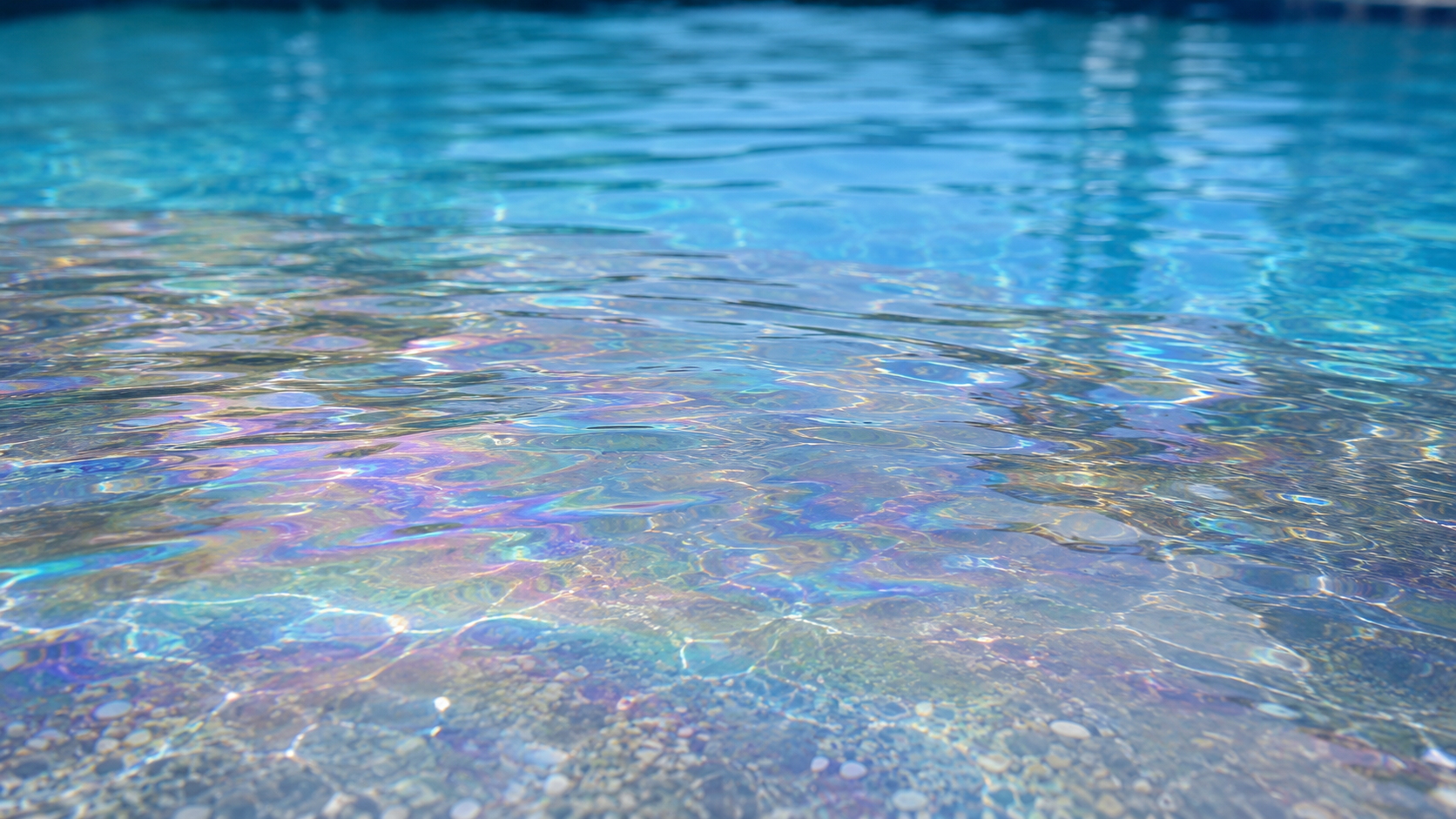 Pool water looks oily shown by a subtle iridescent surface sheen reflecting rainbow colors across clear blue water in an Orlando pool.